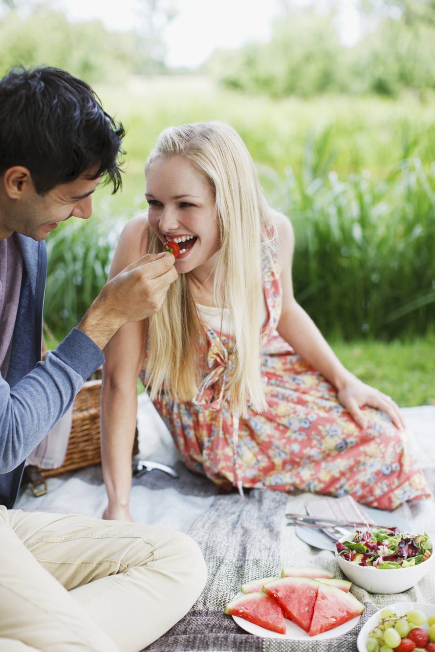 Man feeding woman strawberry on picnic blanket in park