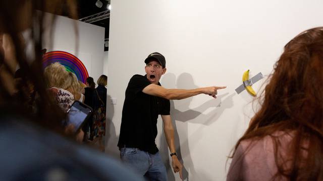 FILE PHOTO: A man poses for a photo next to a banana attached with duct-tape that replaces the artwork 'Comedian' by the artist Maurizio Cattelan, which was eaten by David Datuna, in Miami Beach