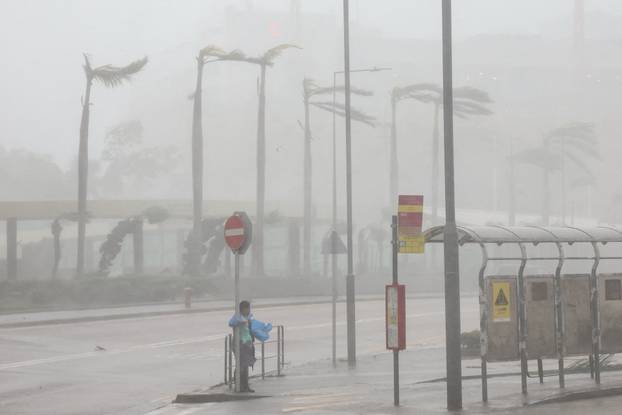 A woman clings to a traffic sign to maintain balance against strong winds from Super Typhoon Ragasa in Hong Kong