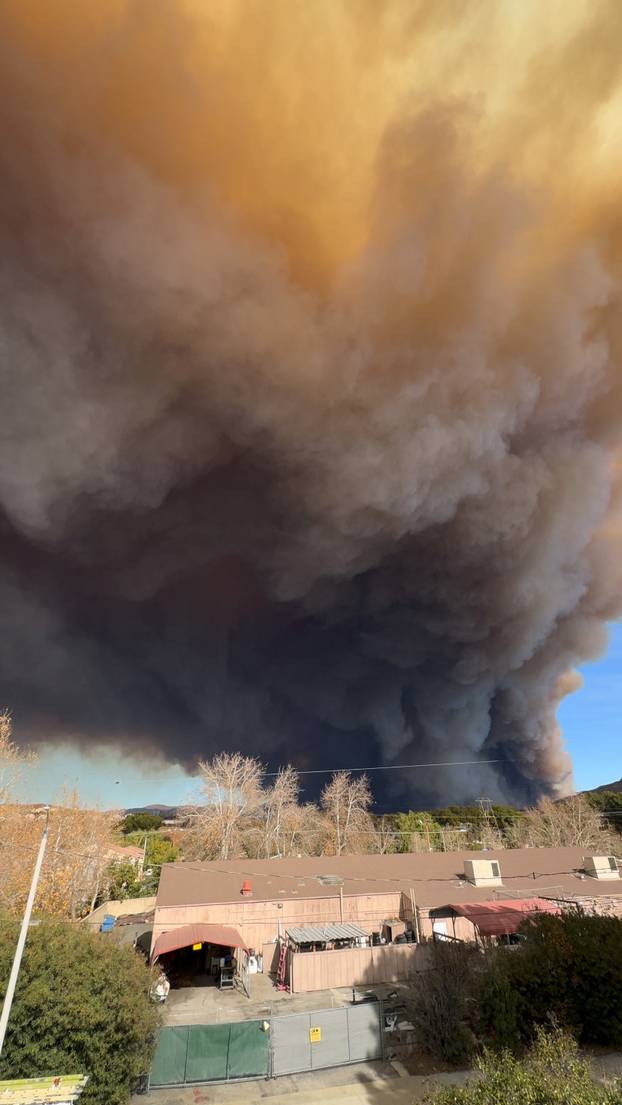 Smoke rises above a building in a residential area as the Hughes Fire burns, as seen from Castaic