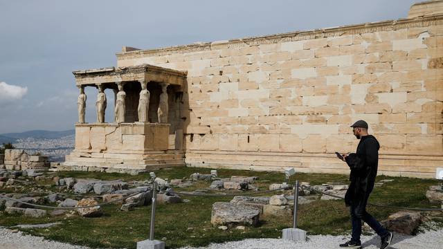 A tourist walks past the Erechtheion temple atop the Acropolis hill in Athens