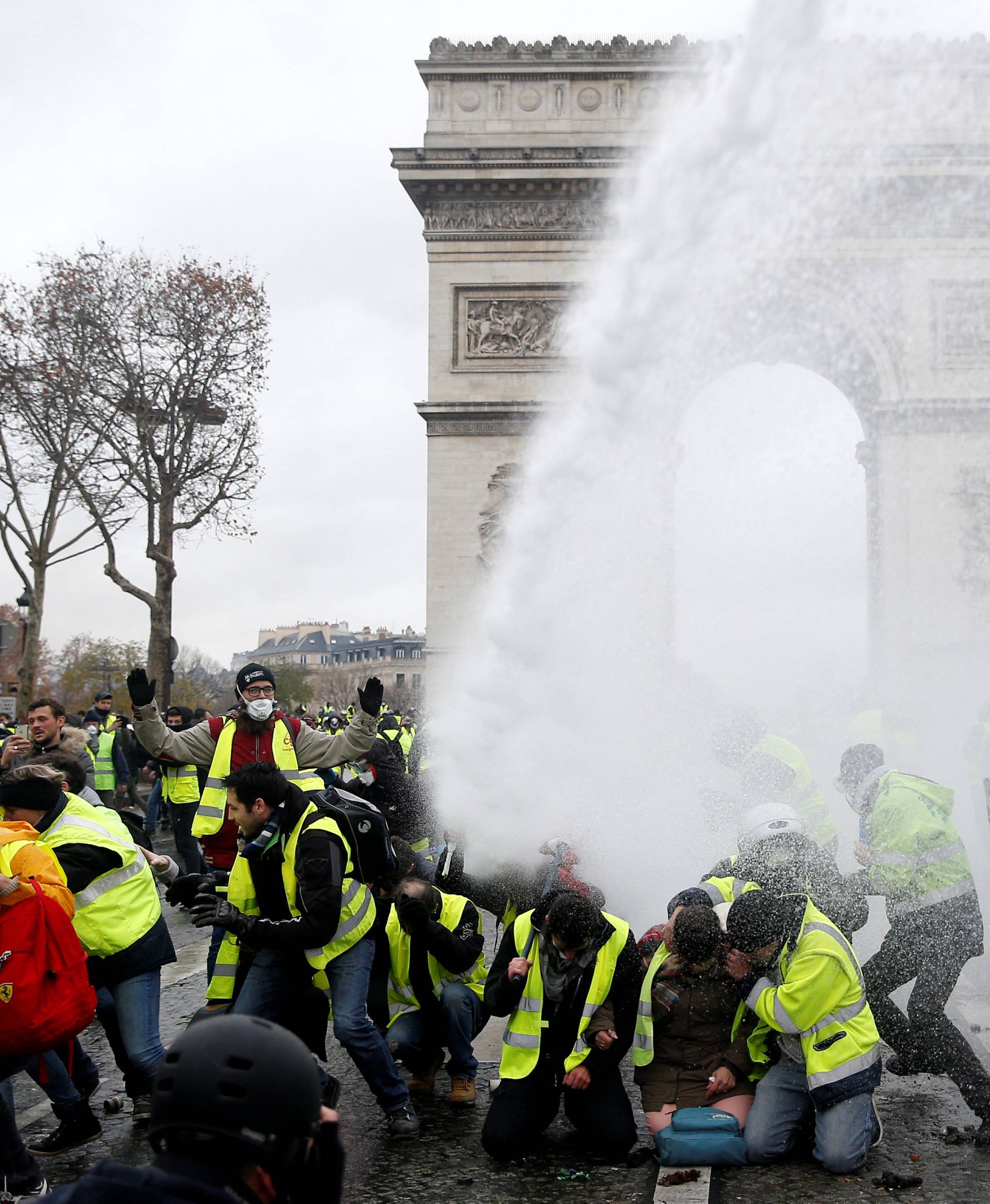 Protesters wearing yellow vests, a symbol of a French drivers' protest against higher diesel taxes,  stand up in front of a police water canon during clashes near the Arc de Triomphe in Paris