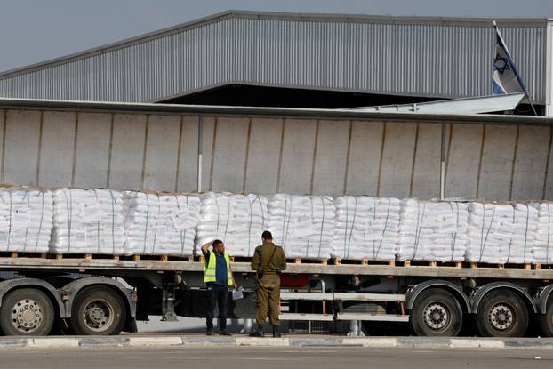 An Israeli security forces member speaks to a worker next to a truck carrying aid at the Kerem Shalom crossing between Israel and Gaza, before going into Gaza, on the Israeli side of the Israel-Gaza border
