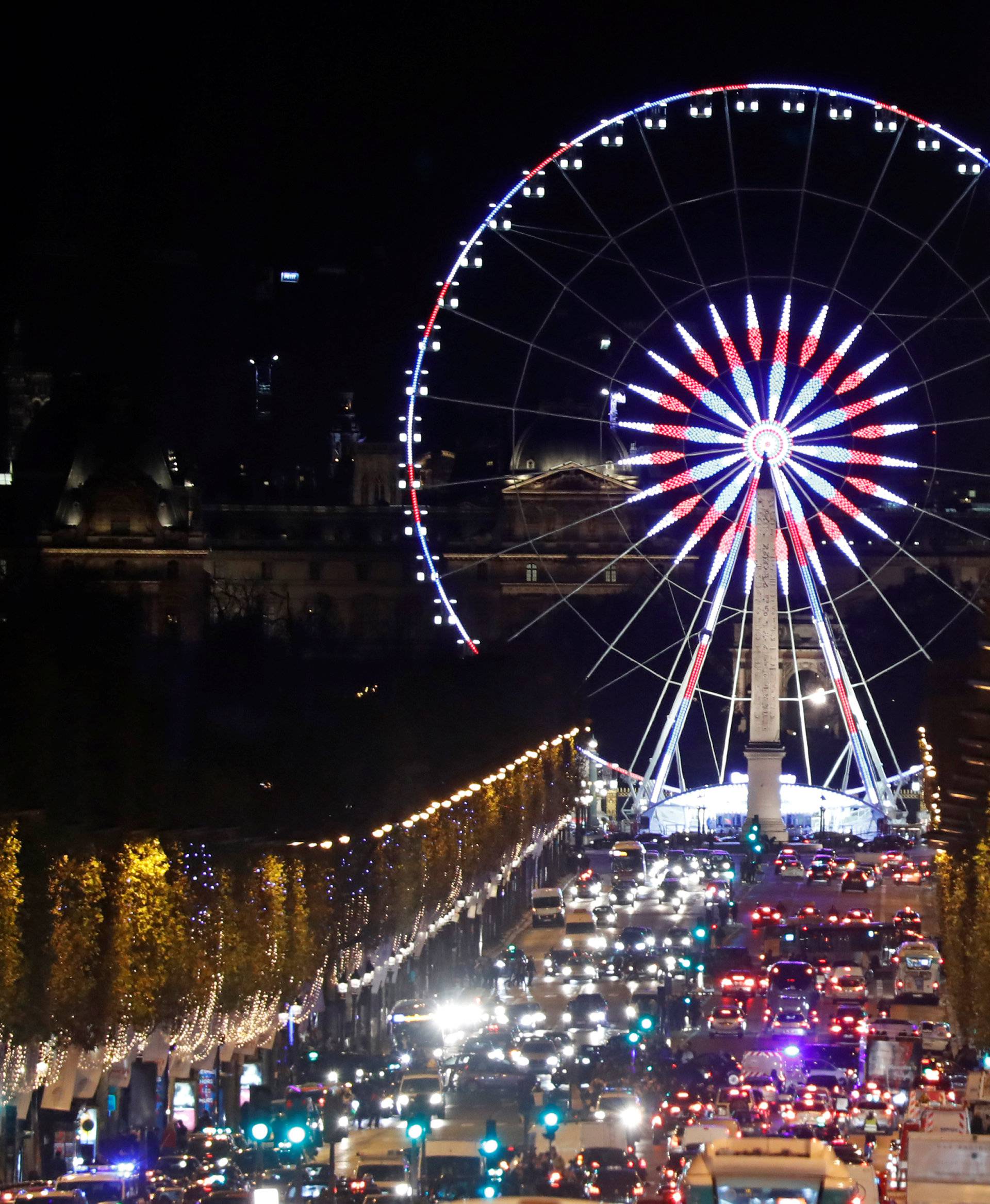 Christmas holiday lights hang from trees to illuminate Champs Elysees avenue in Paris as rush hour traffic fills the avenue leading down to the Giant Ferris Wheel at place de la Concorde in Paris