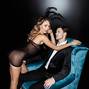 Sexy woman in bunny ears looking at camera near man in suit sitting in armchair on black background