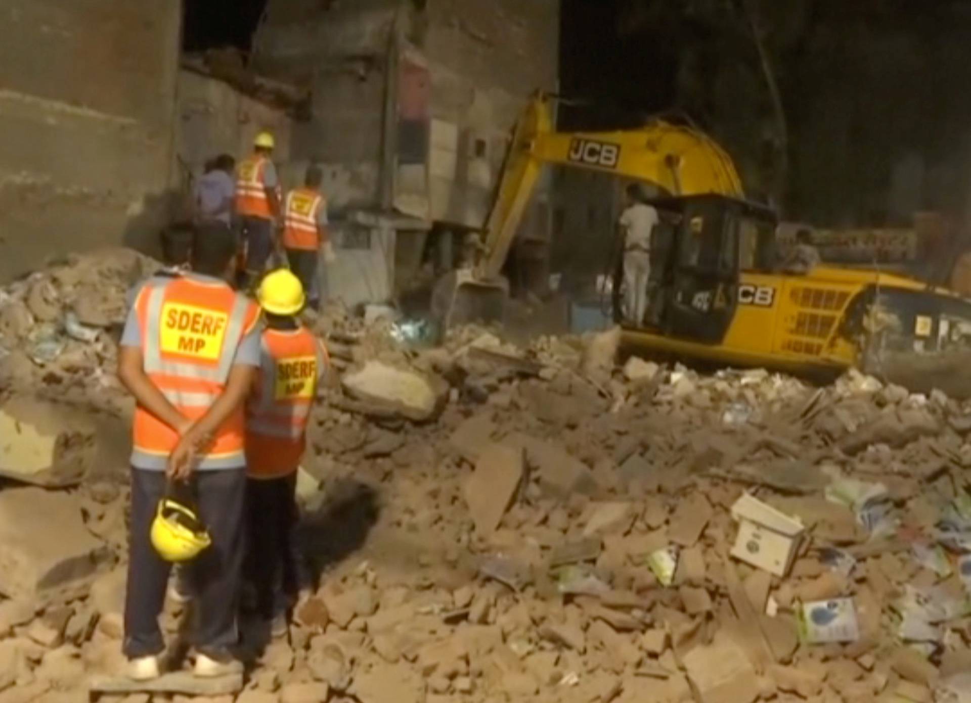 Still image of workers watching as an excavator clears the debris after a hotel collapsed in Indore