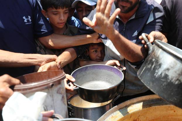 Palestinians wait to receive food cooked by a charity kitchen, in Gaza City