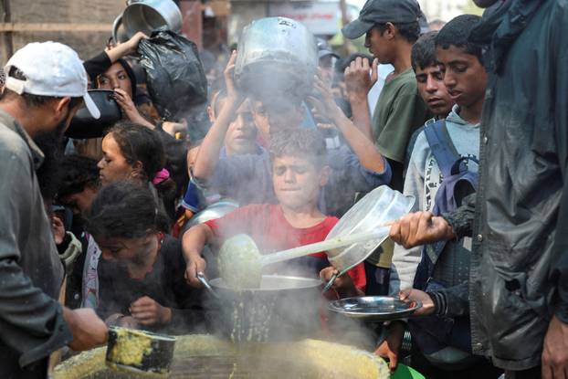 Palestinians gather to receive meals cooked by a charity kitchen, in Deir Al-Balah, central Gaza Strip