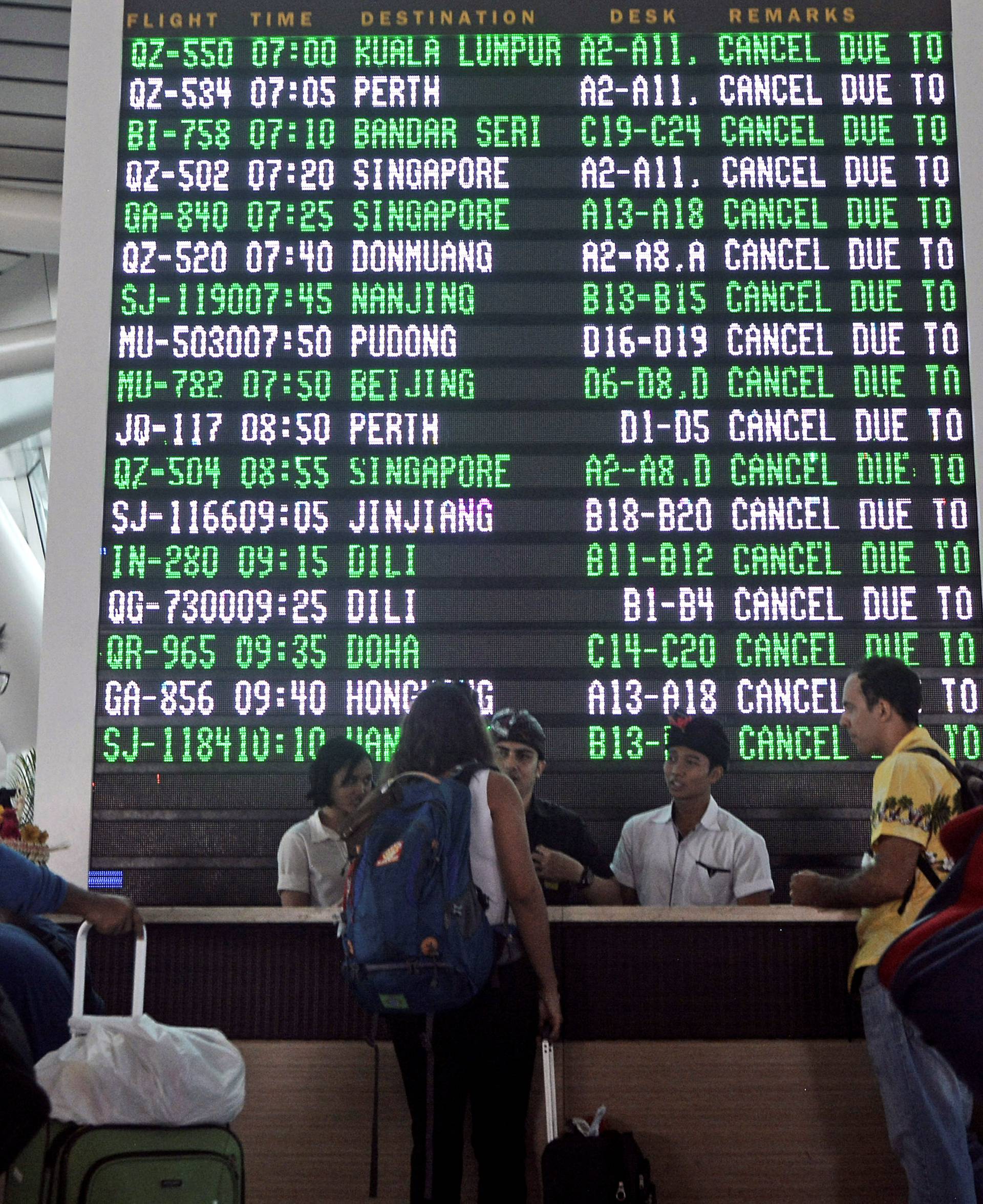 Passengers ask staff about their flights near the flight screen after Ngurah Rai airport closed their operation due to eruption of Mount Agung in Bali resort island