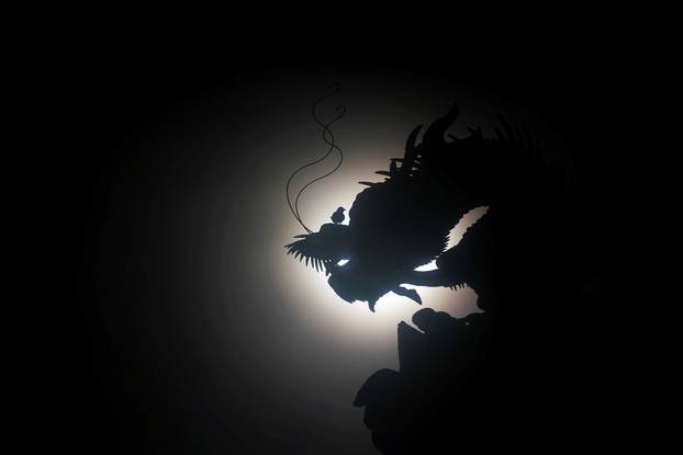 A bird sits on a dragon sculpture at a temple during a solar eclipse at Budai township,