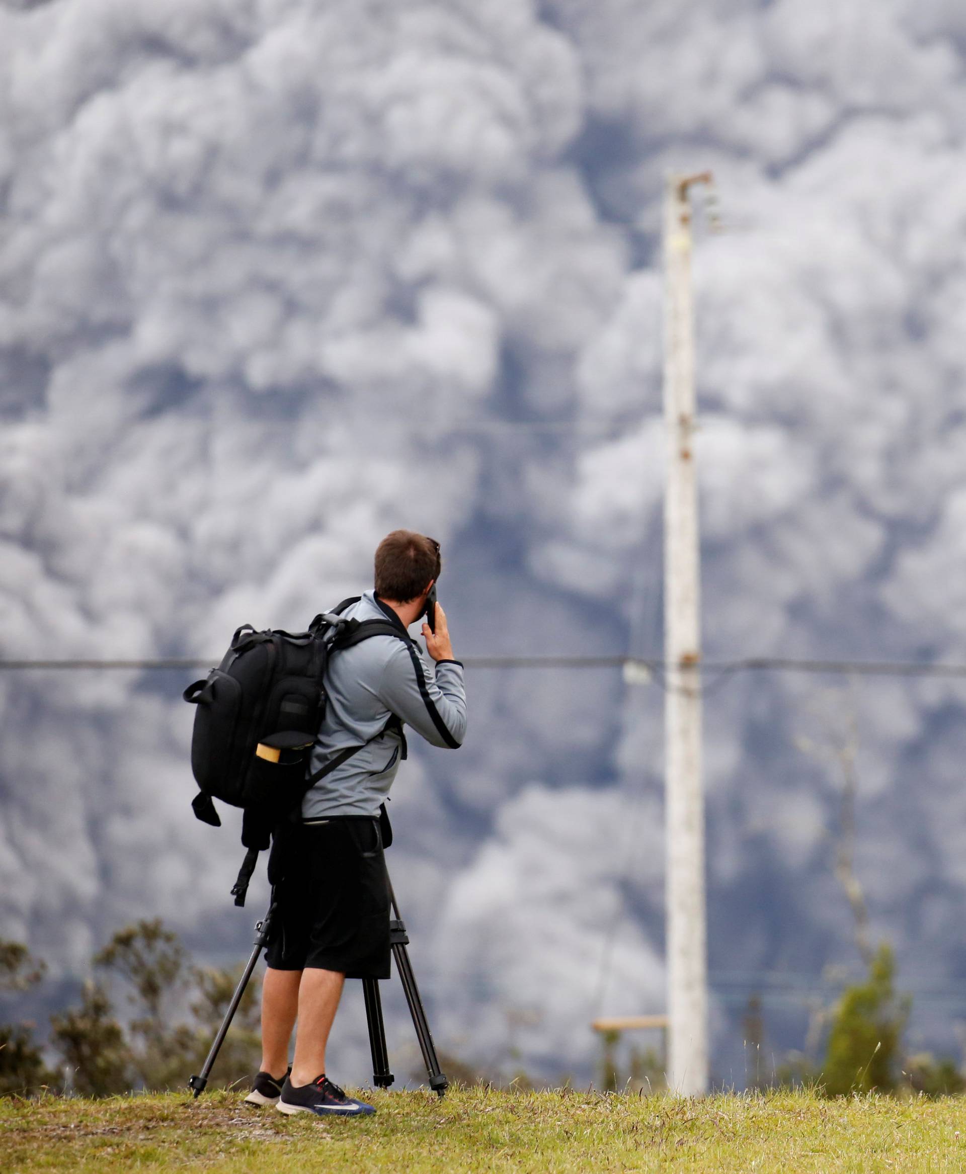 People watch as ash erupt from the Halemaumau crater near the community of Volcano