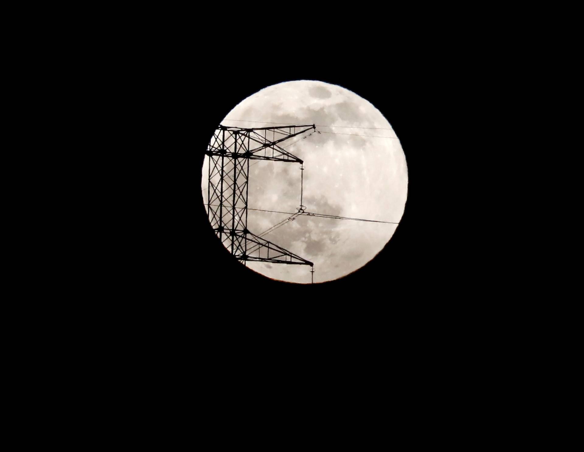 The full moon is seen rising behind an electric tower during the penumbral lunar eclipse in Ronda, near Malaga