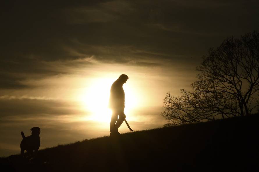 A man walks his dog in front of the setting sun on Primrose Hill in London