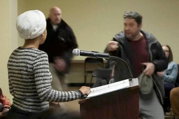 A man shouts at U.S. Rep. Ilhan Omar after spraying her, during a town hall meeting in Minneapolis