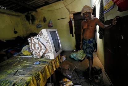 A man stands near a damaged computer monitor inside a house which was affected by the floods in Biyagama