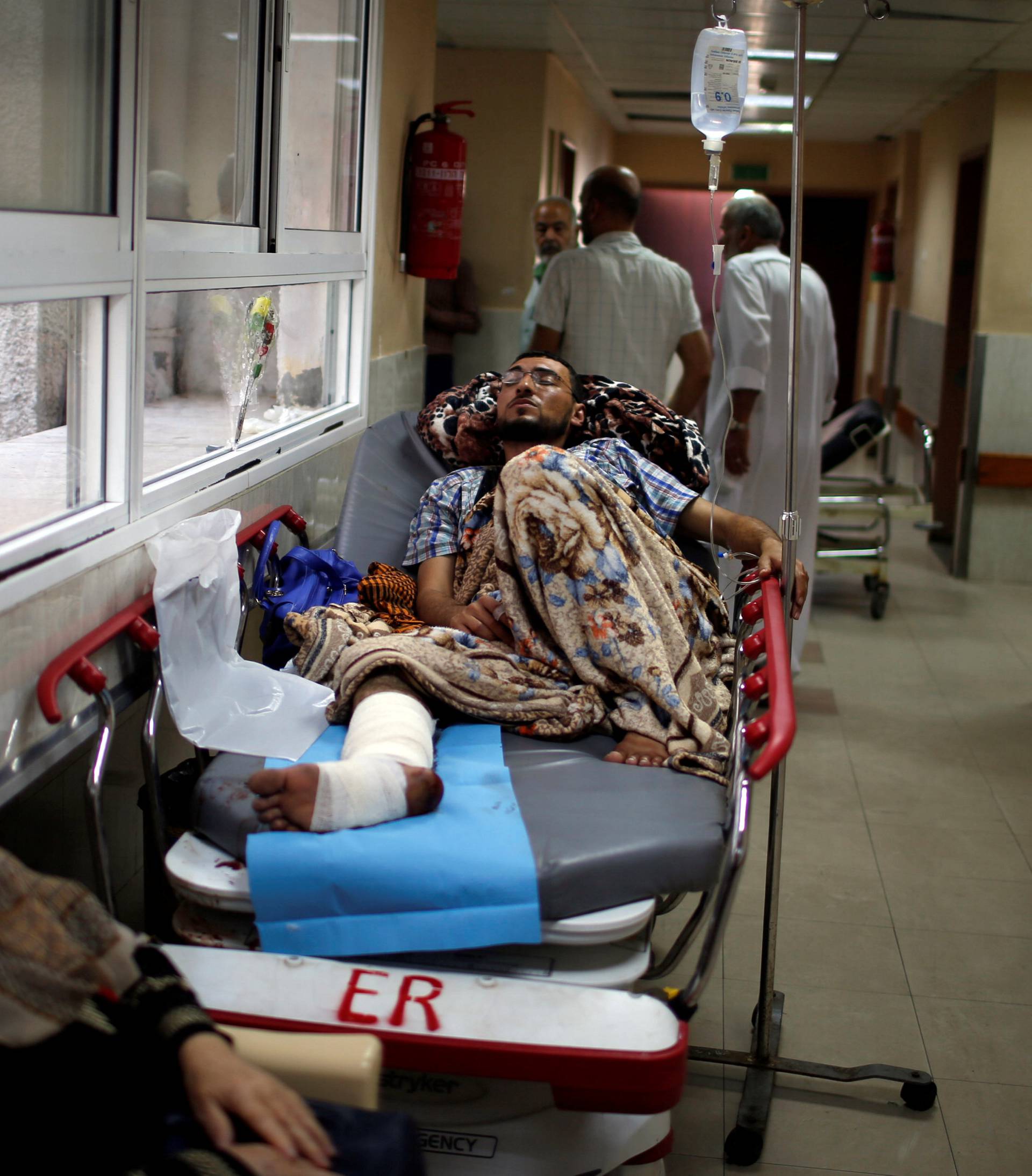 Injured Palestinian lies on a bed in the corridor of a hospital in Gaza City