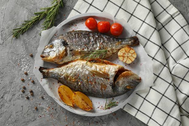 Plate with baked Dorado on garnished grey background, top view