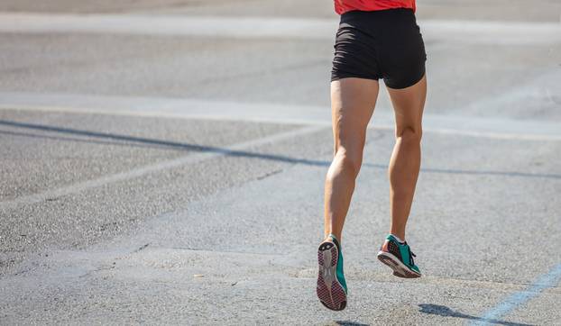 Running in the city roads. Young man runner, back view, blur background, copy space
