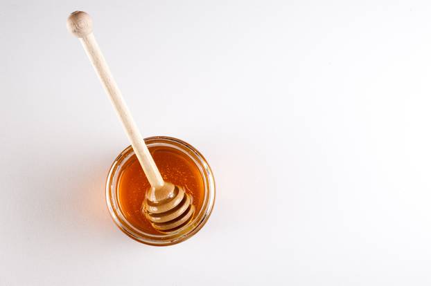 Glass can full of honey and wooden stick in it. top view