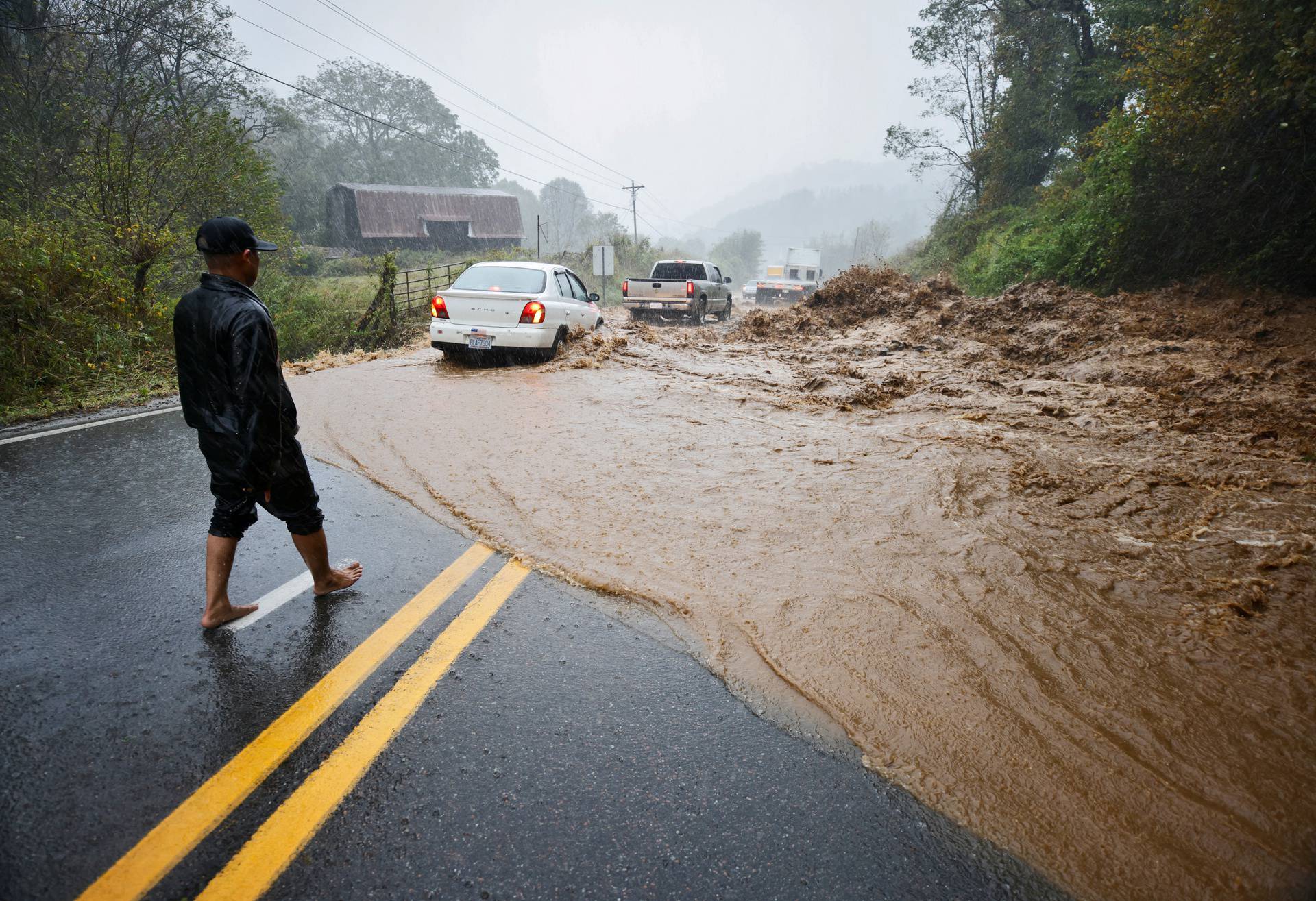 A resident watches cars traverse on a flooded road as Tropical Storm Helene strikes Boone, North Carolina