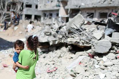 A Palestinian girl carries a boy amid the rubble of their houses destroyed by Israeli air strikes