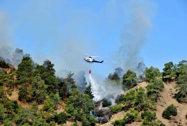 A firefighting helicopter drops water onto a forest fire at the foothills of Troodos mountain region in Cyprus