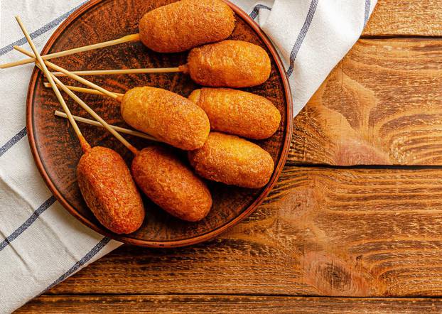 American street food concept. Corn dogs with mustard and ketchup on wooden background. Overhead, copy space