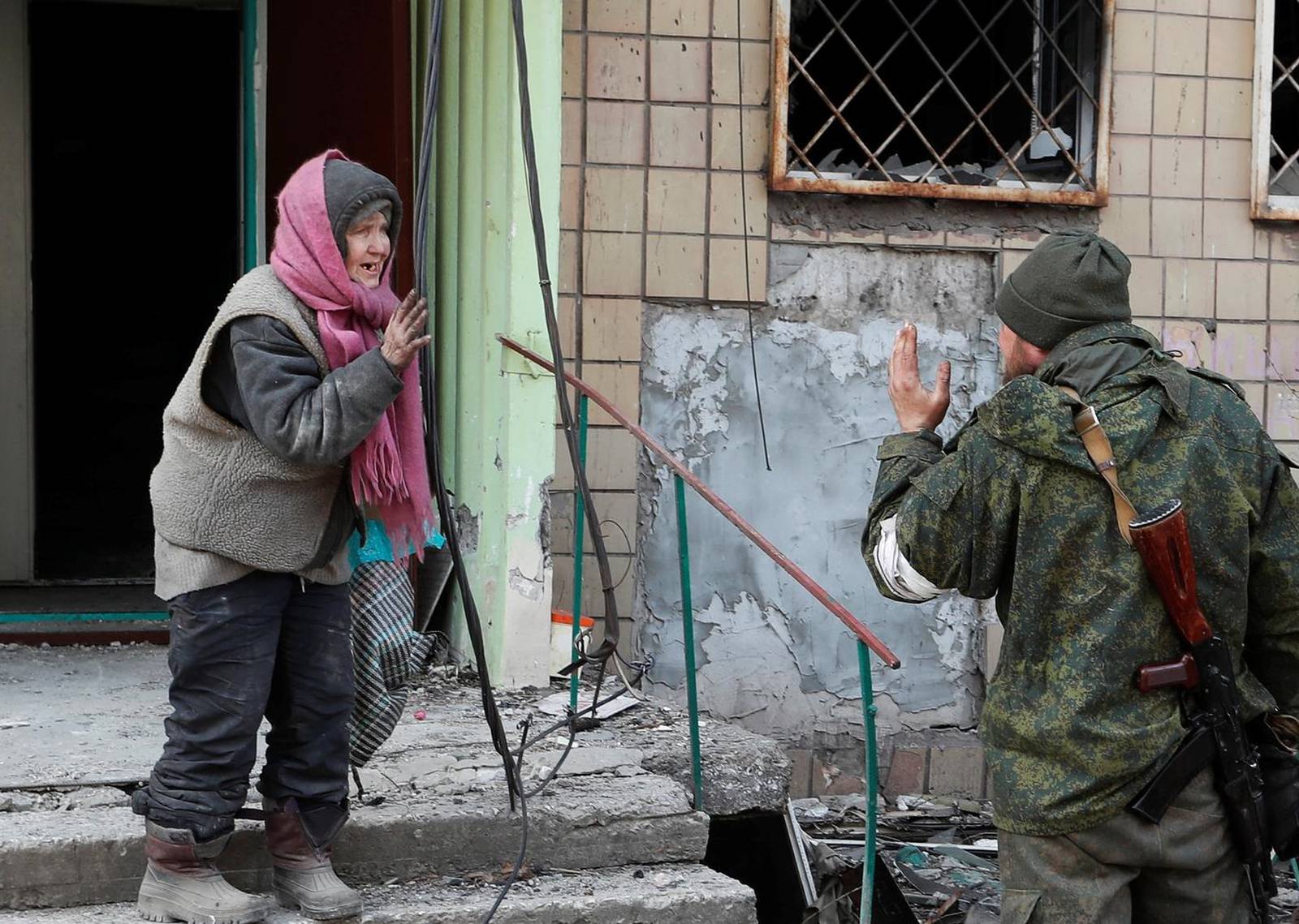 A local resident speaks to a service member of pro-Russian troops outside a damaged apartment building in Mariupol