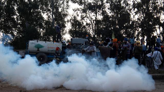 Farmers attempt to cover tear gas shells fired by police to disperse them, at Shambhu