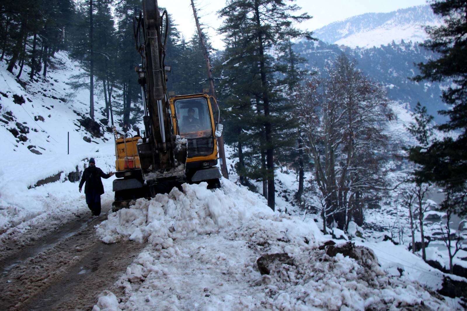 A man guides an excavator operator as they clear snow-covered road to make way to reach the areas affected by heavy snowfall and avalanches, in Neelum Valley
