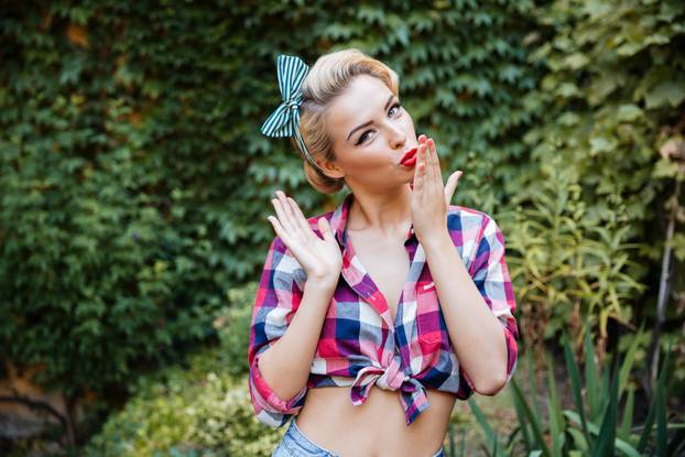 Happy attractive pinup girl sending a kiss in the garden