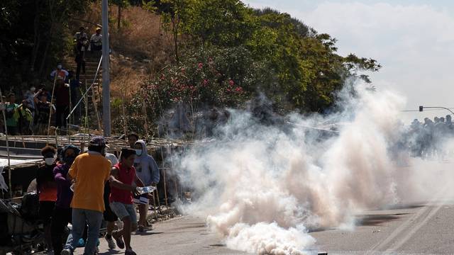 Refugees and migrants flee tear gas fired by riot police during clashes, on the island of Lesbos