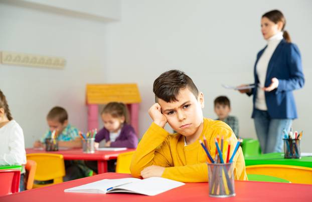 Portrait,Of,Upset,Boy,In,Schoolroom,On,Background,With,Pupils