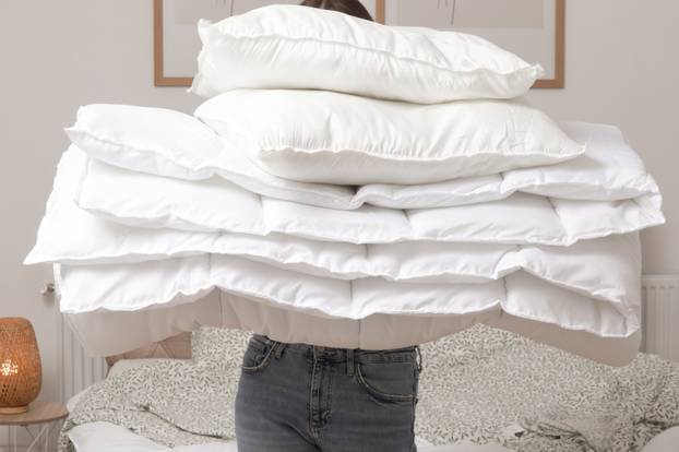 Woman,Holding,Pile,Of,Soft,White,Folded,Duvet,And,Pillows
