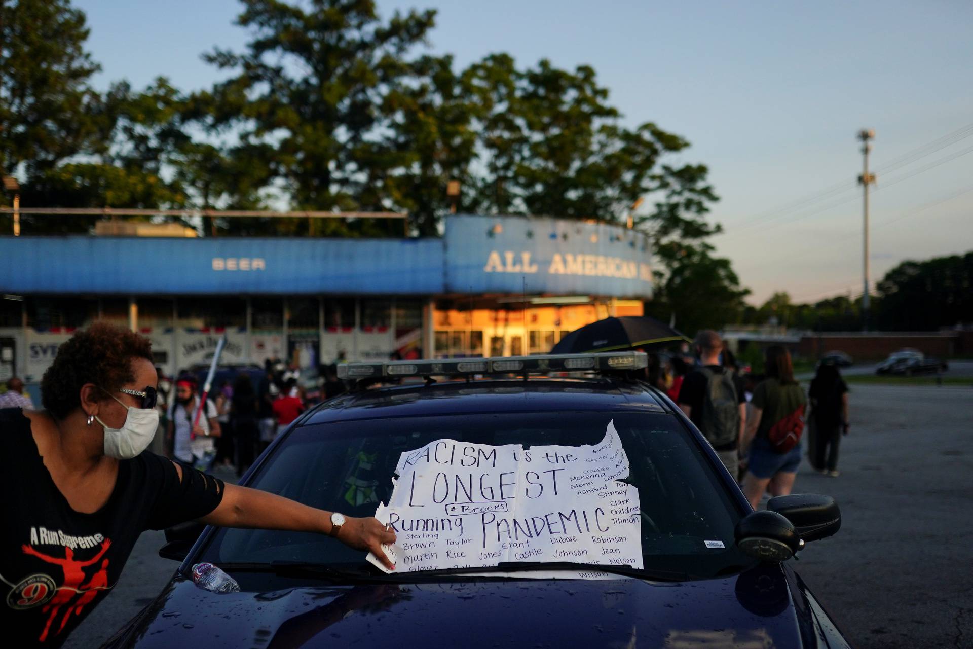 A woman adjusts a protest sign that was placed under the windshield wiper of a police car during a rally against racial inequality and the police shooting death of Rayshard Brooks, in Atlanta