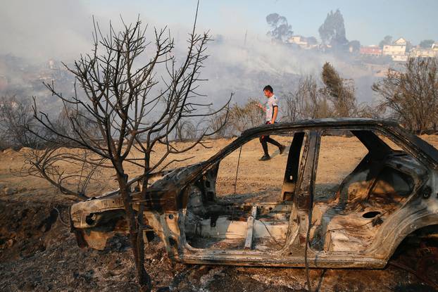 A resident is seen next to a burned car in front of dozens of houses burned on a hill, due to a forest fire but there have been no reports of death, local authorities said in Valparaiso, Chile