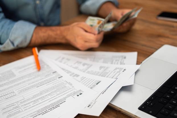 Man,In,Denim,Shirt,Counting,Cash,While,Examining,Tax,Forms