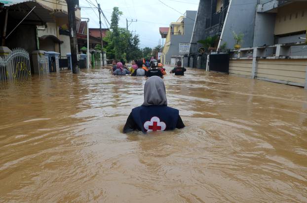 A volunteer wades through floods at a residential area in Makassar