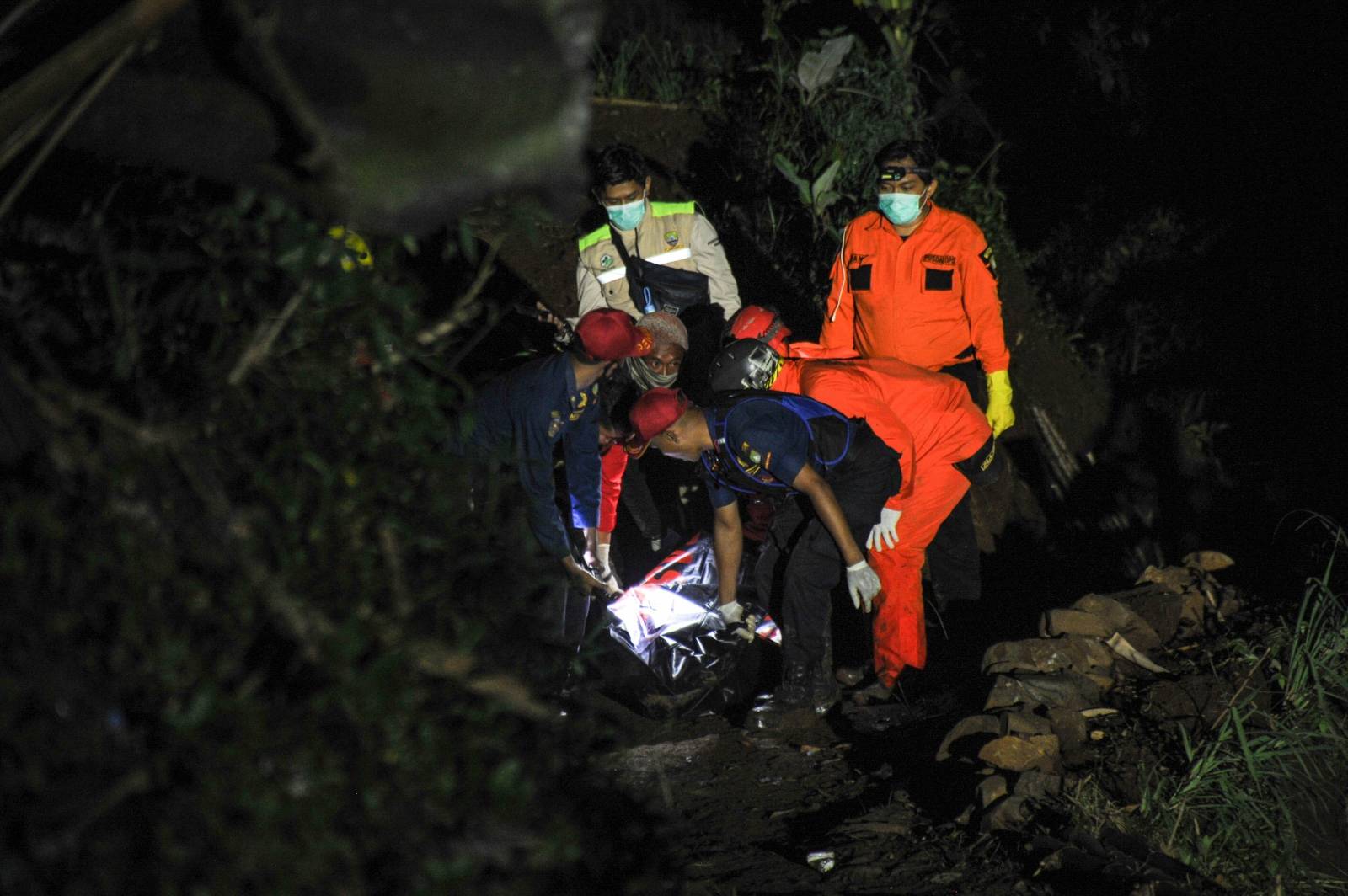 Rescue personnel carry a body bag containing a victim of a bus that fell into a ravine in Sumedang, Indonesia