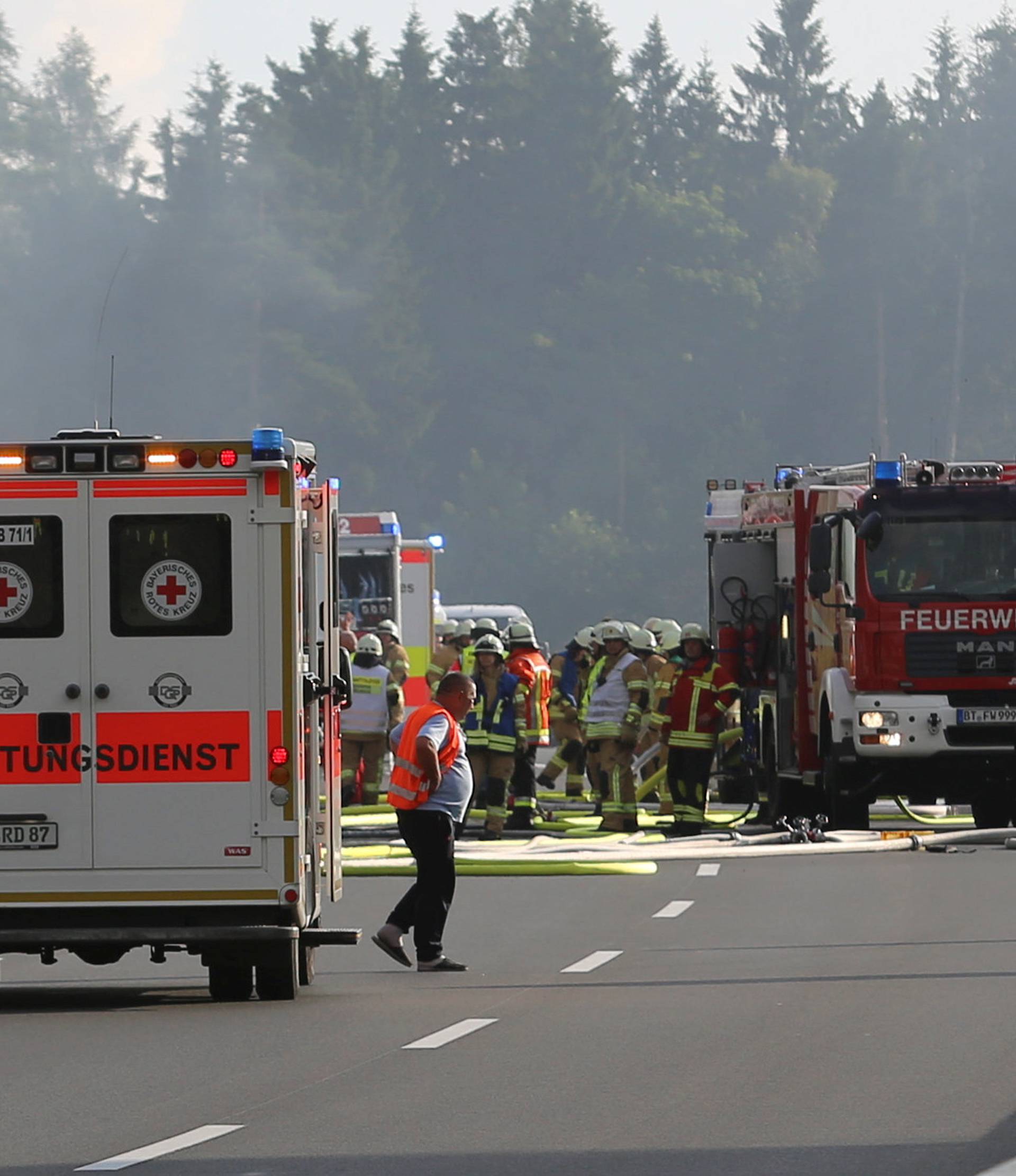 Ambulance cars and fire engines near a bus where a coach burst into flames after colliding with a lorry on a motorway near Muenchberg