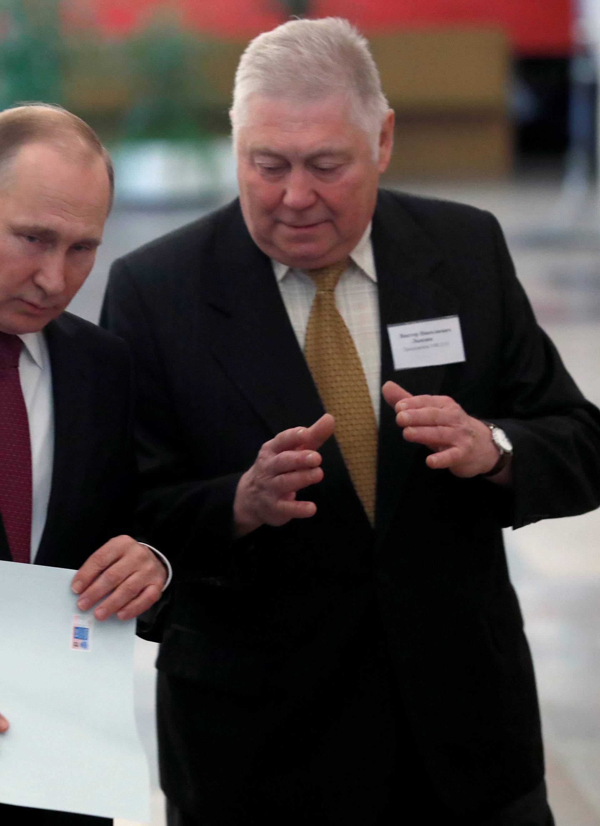 Russian President and Presidential candidate Vladimir Putin talks to a member of a local election commission at a polling station during the presidential election in Moscow