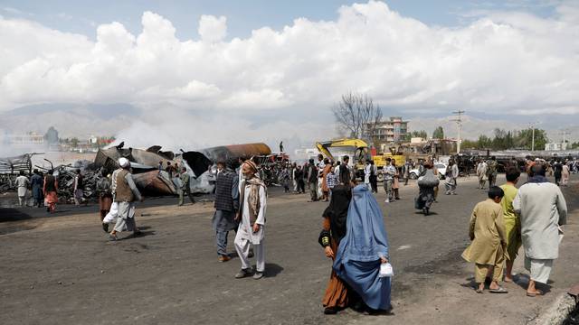 People walk past burnt fuel tankers and trucks after an overnight fire, on the outskirts of Kabul