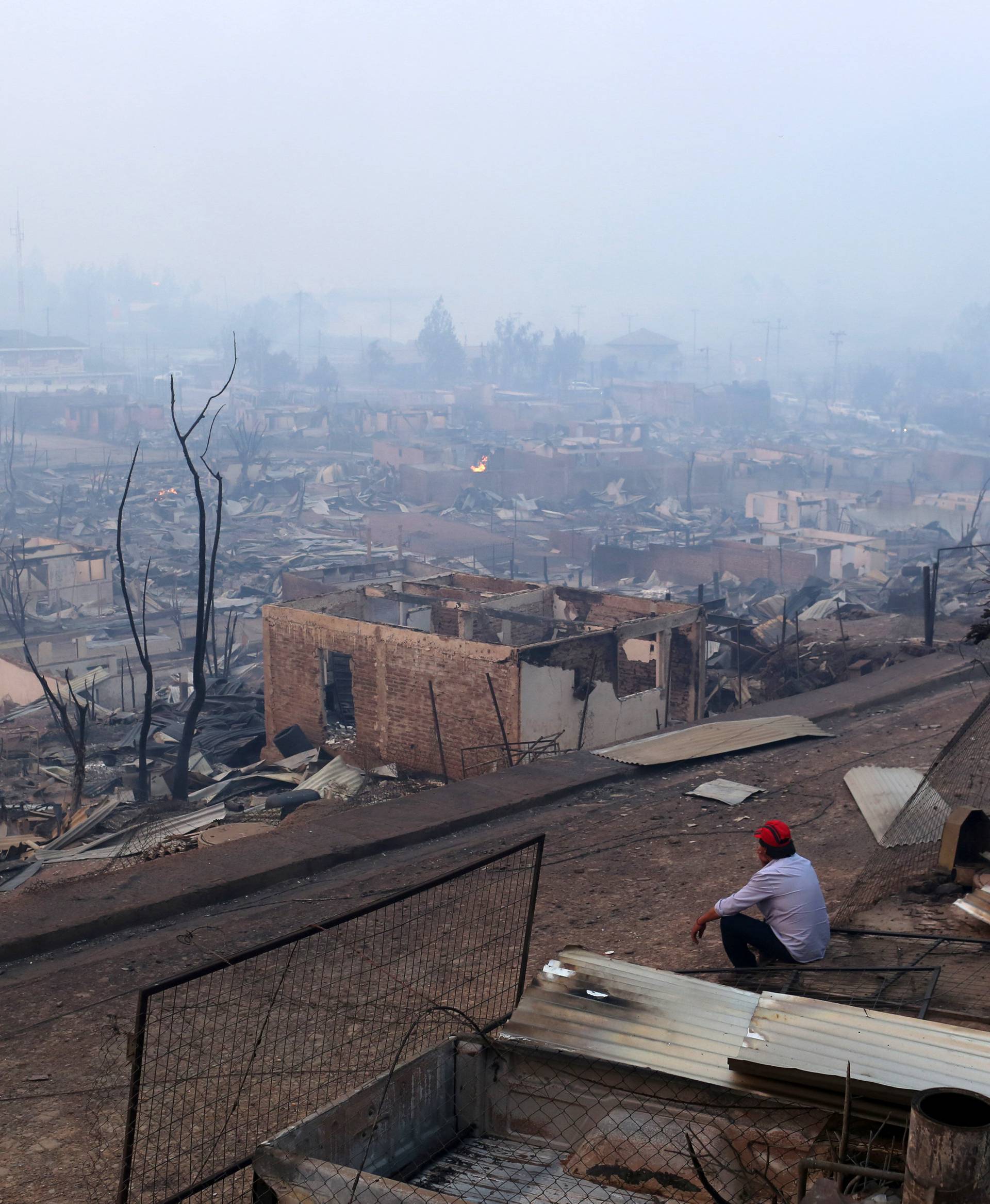 A man sits next to the remains of burnt houses as the worst wildfires in Chile's modern history ravage wide swaths of the country's central-south regions, in Santa Olga