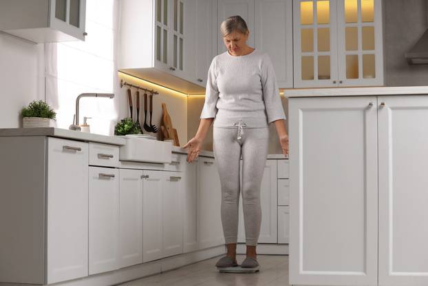 Menopause, weight gain. Concerned woman standing on floor scales