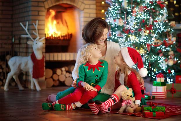 Family with kids at Christmas tree and fireplace. Mother and chi