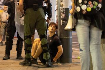 Serbian police officers stand next to a detained protester during standoff  between ruling party supporters and anti-government protesters in Belgrade