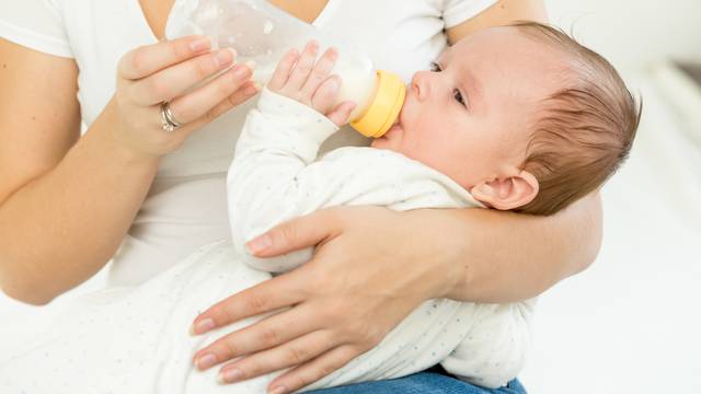 Mother giving milk from bottle to her baby sleeping on hands