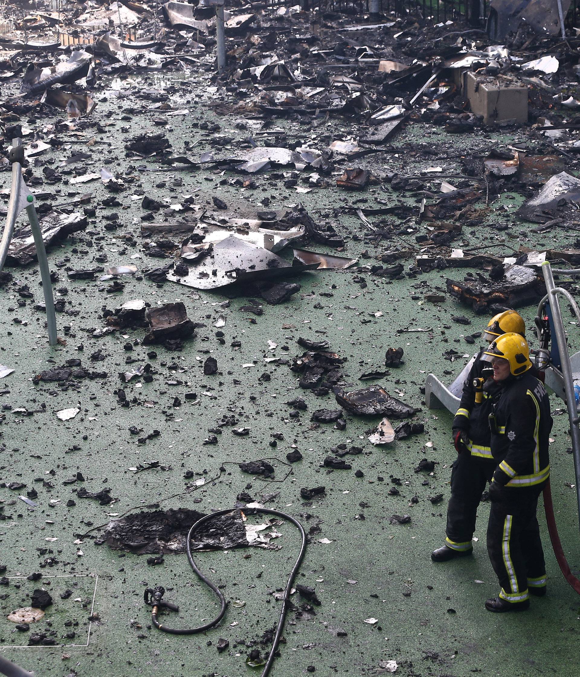 Firefighters stand amid debris in a childrens playground near a tower block severly damaged by a serious fire, in north Kensington, West London