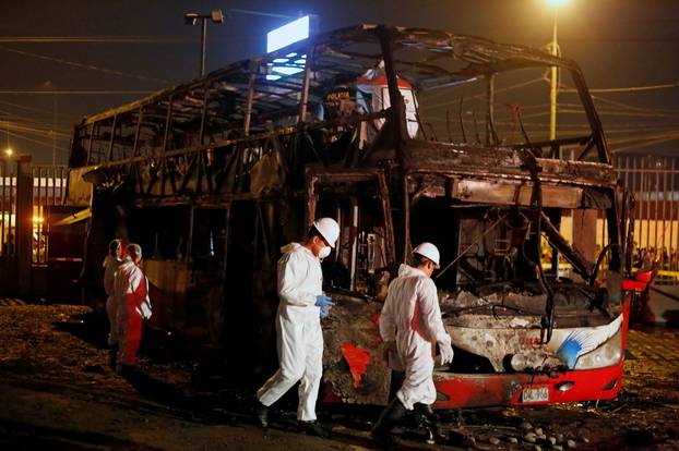 Peruvian investigators work next to a burnt bus on a street in Lima