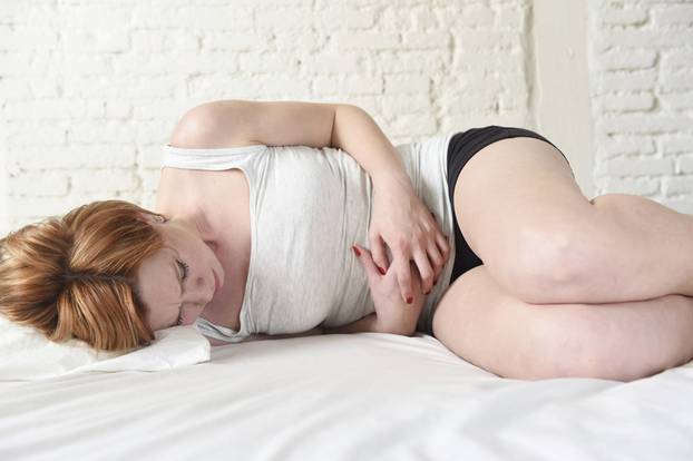 young beautiful woman suffering stomach cramps on belly holding tummy with her hands in period pain